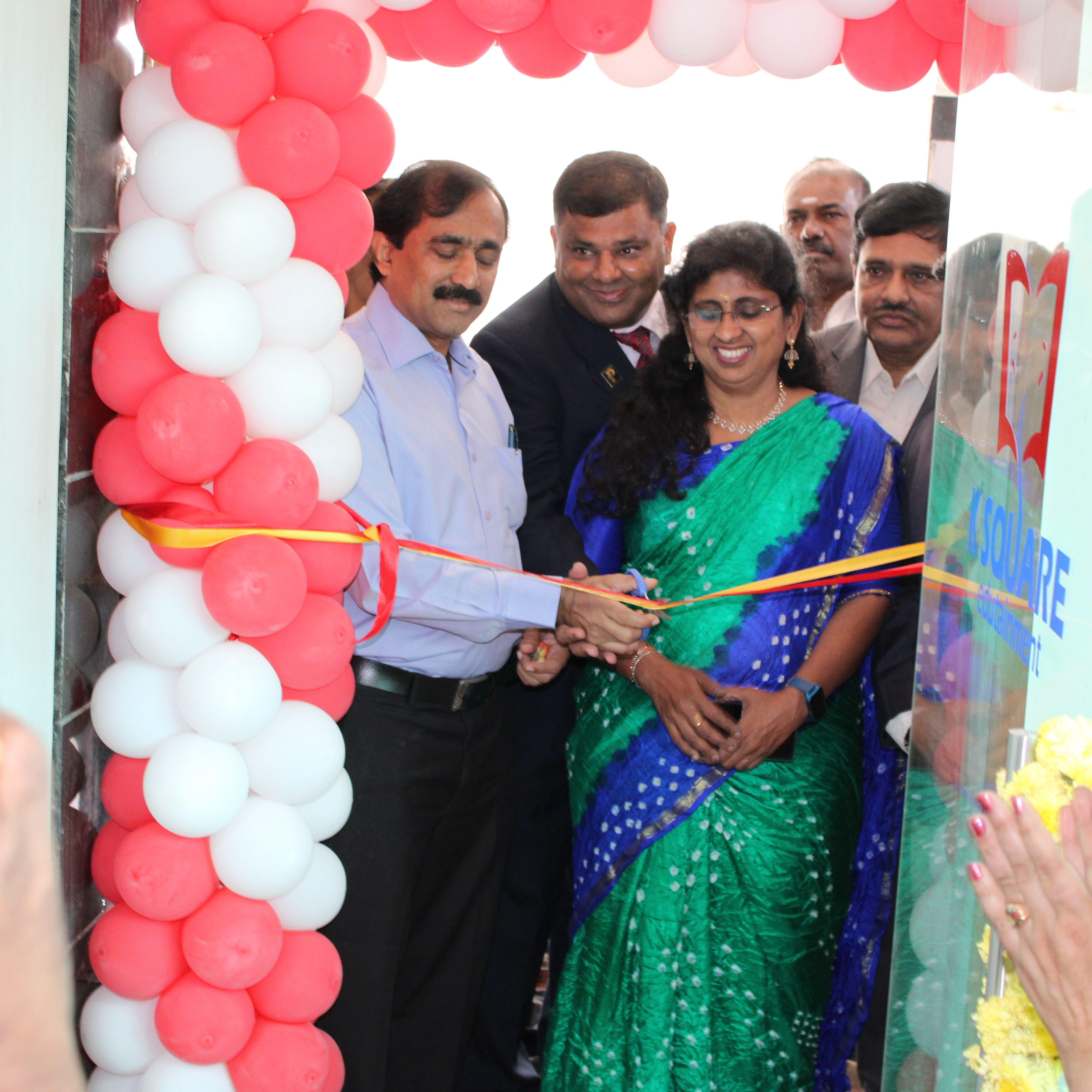 A woman and a man cut a ribbon at an K square edutainment office opening ceremony, symbolizing the start of an event.