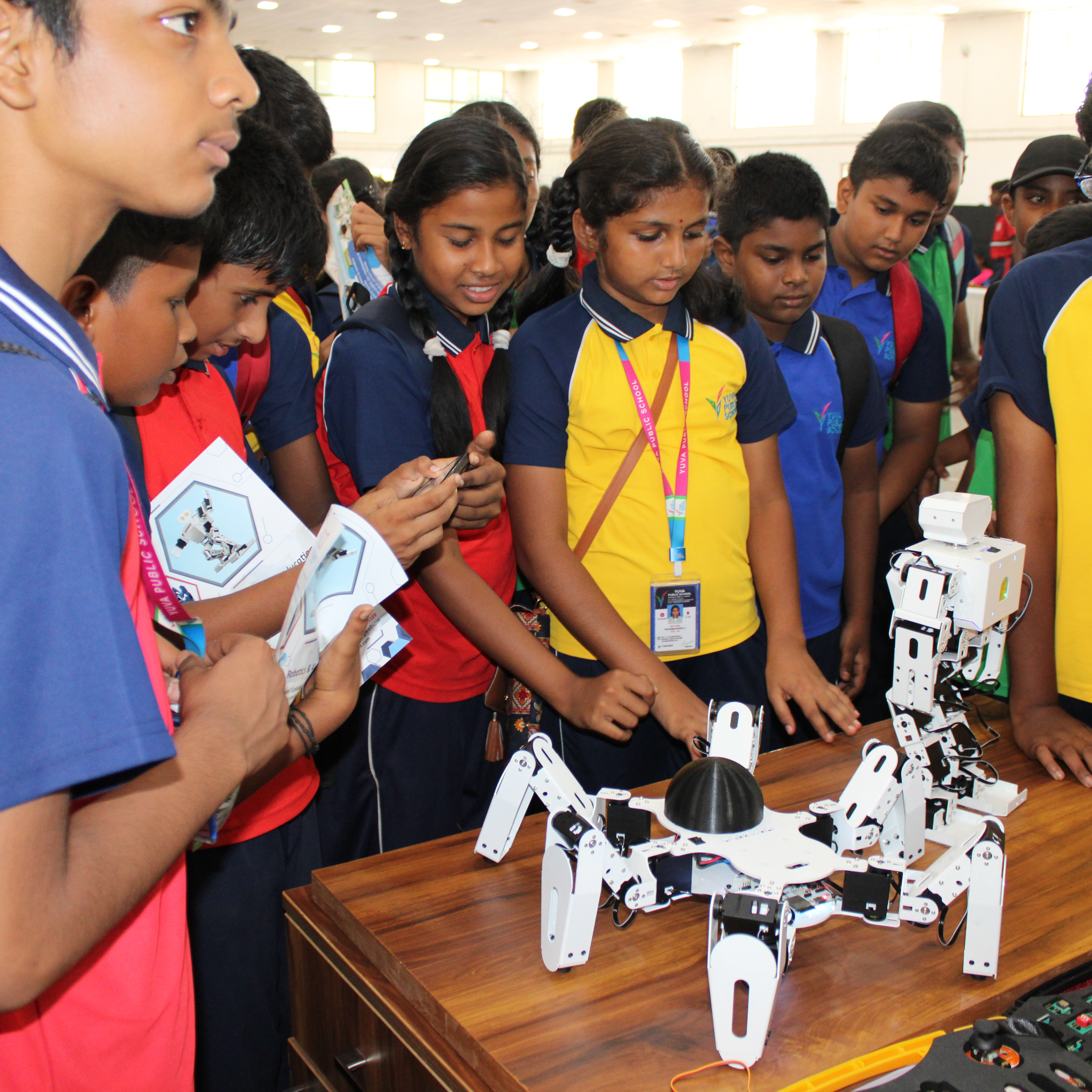 A group of children gathered around a table, observing a K square edutainment robot with curiosity and excitement.