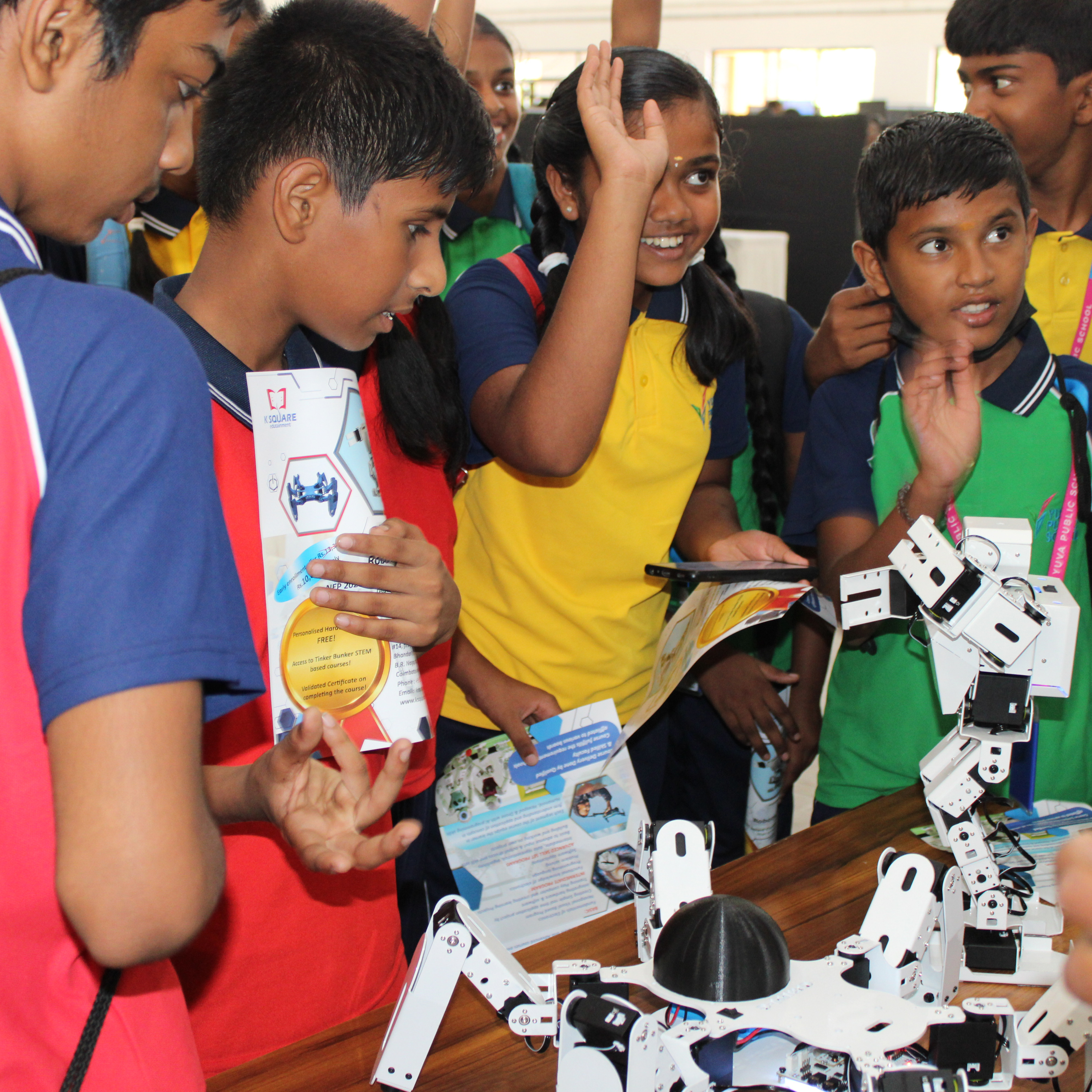 Group of children standing around a table with a K square edutainment robot, exploring STEM concepts together.