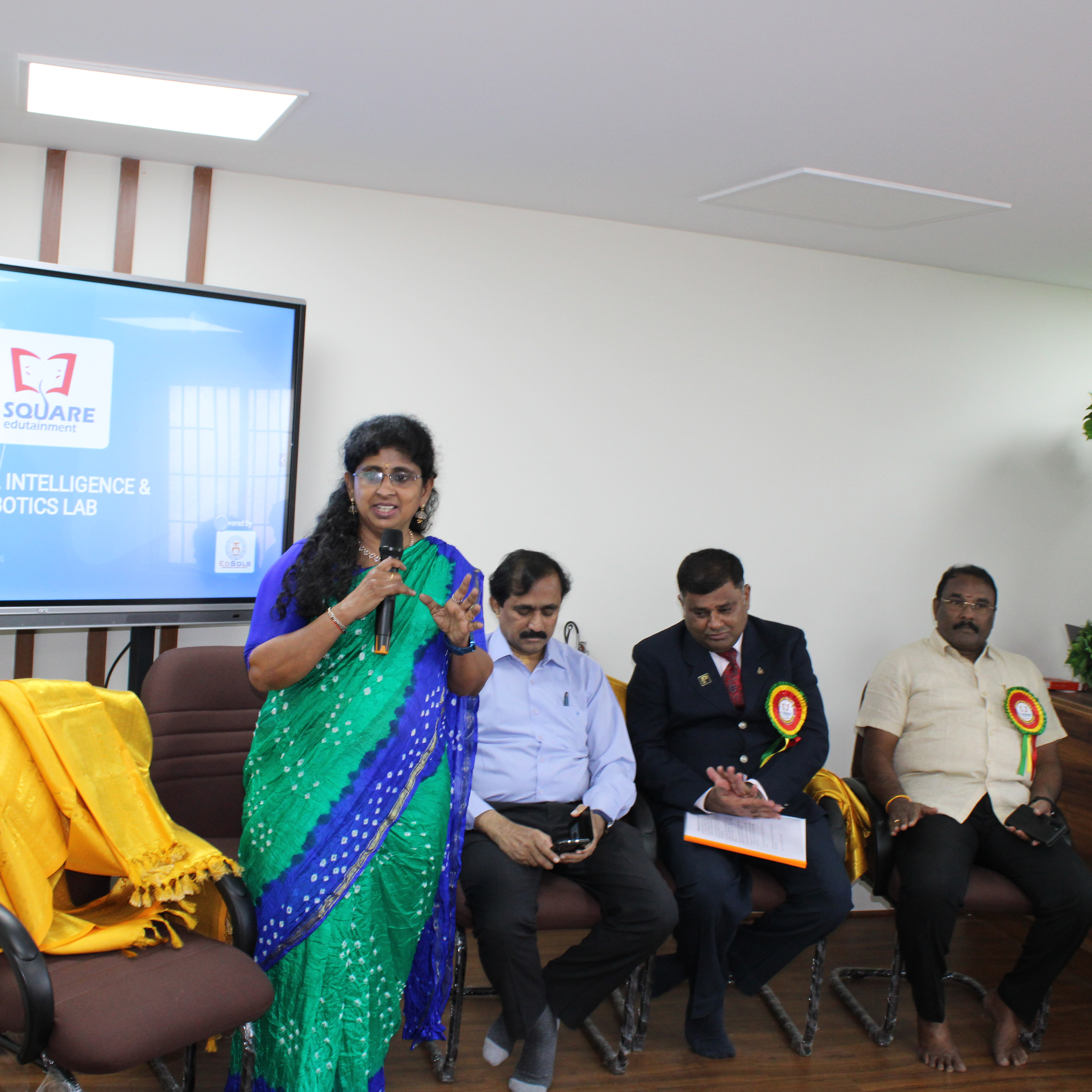 A woman in a sari addresses a gathering of people, engaging them with her words and presence.
