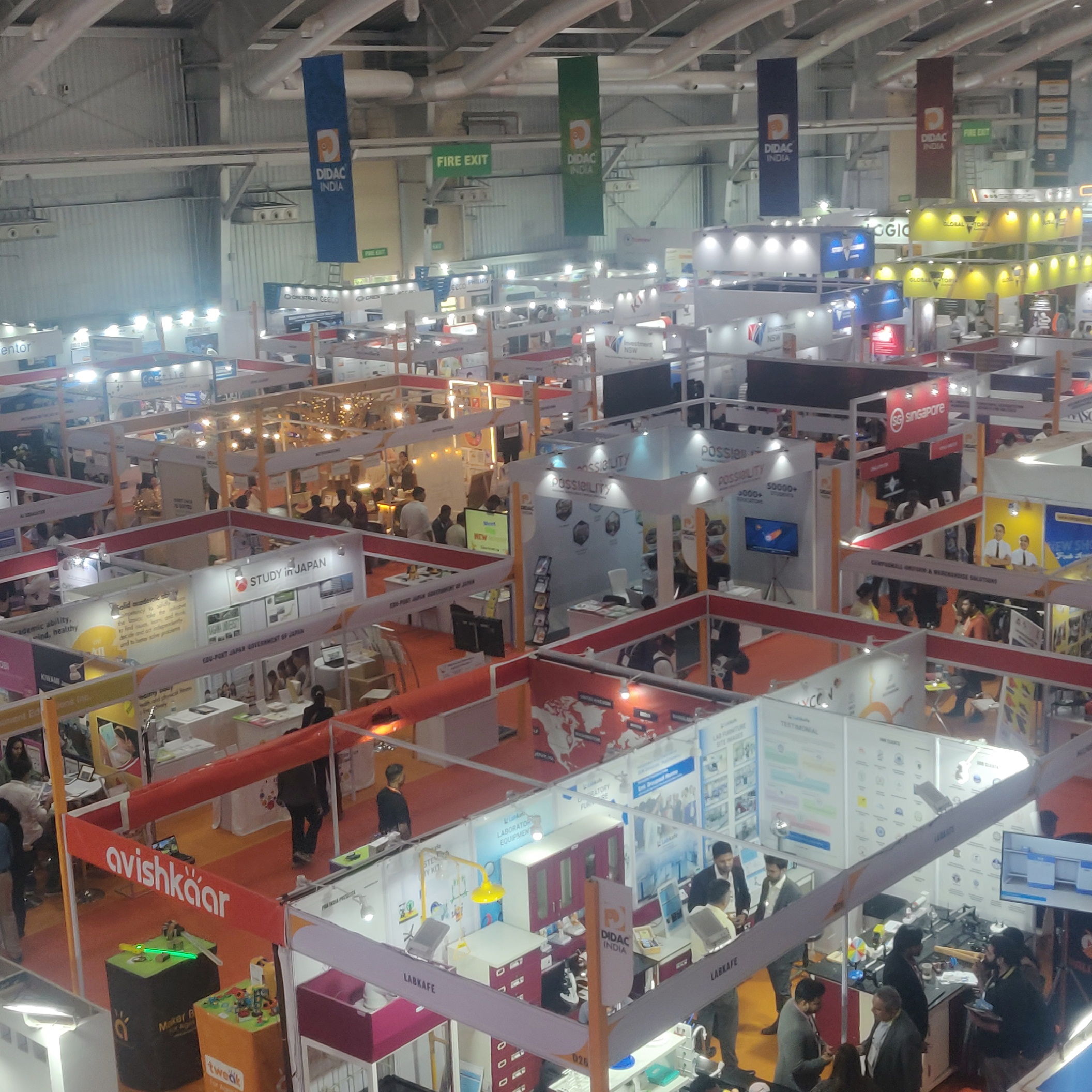 A bustling indoor exhibition hall filled with a diverse crowd of people engaged in various activities.